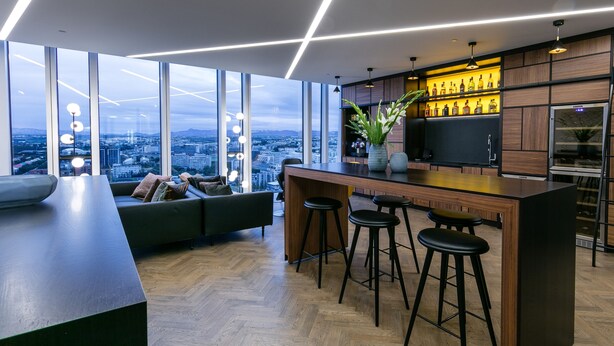 A modern kitchen with a bar area, large windows, and a city view. - Tower Suites Reykjavik (Reykjavik)