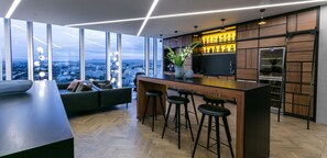 A modern kitchen with a bar area, large windows, and a city view. - Tower Suites Reykjavik (Reykjavik)