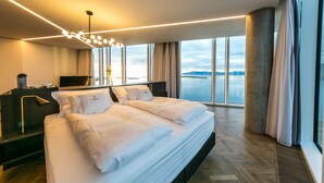 A modern hotel room with a large bed, a desk, and a view of a body of water. - Tower Suites Reykjavik (Reykjavik)