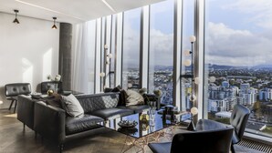 A modern living room with a black leather sofa, a glass coffee table, and a view of a cityscape through large windows. - Tower Suites Reykjavik (Reykjavik)