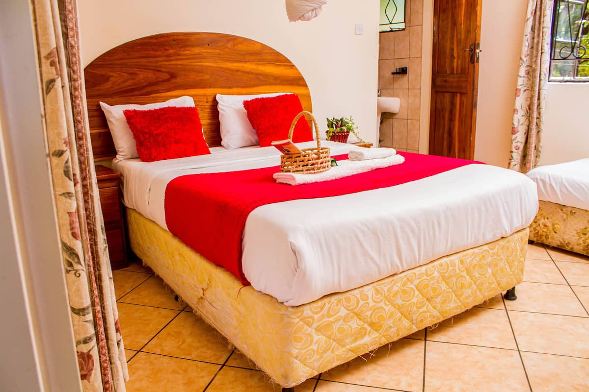 Cama bem arrumada com colcha vermelha e branca, cabeceira de madeira e um pequeno vaso com planta ao lado.