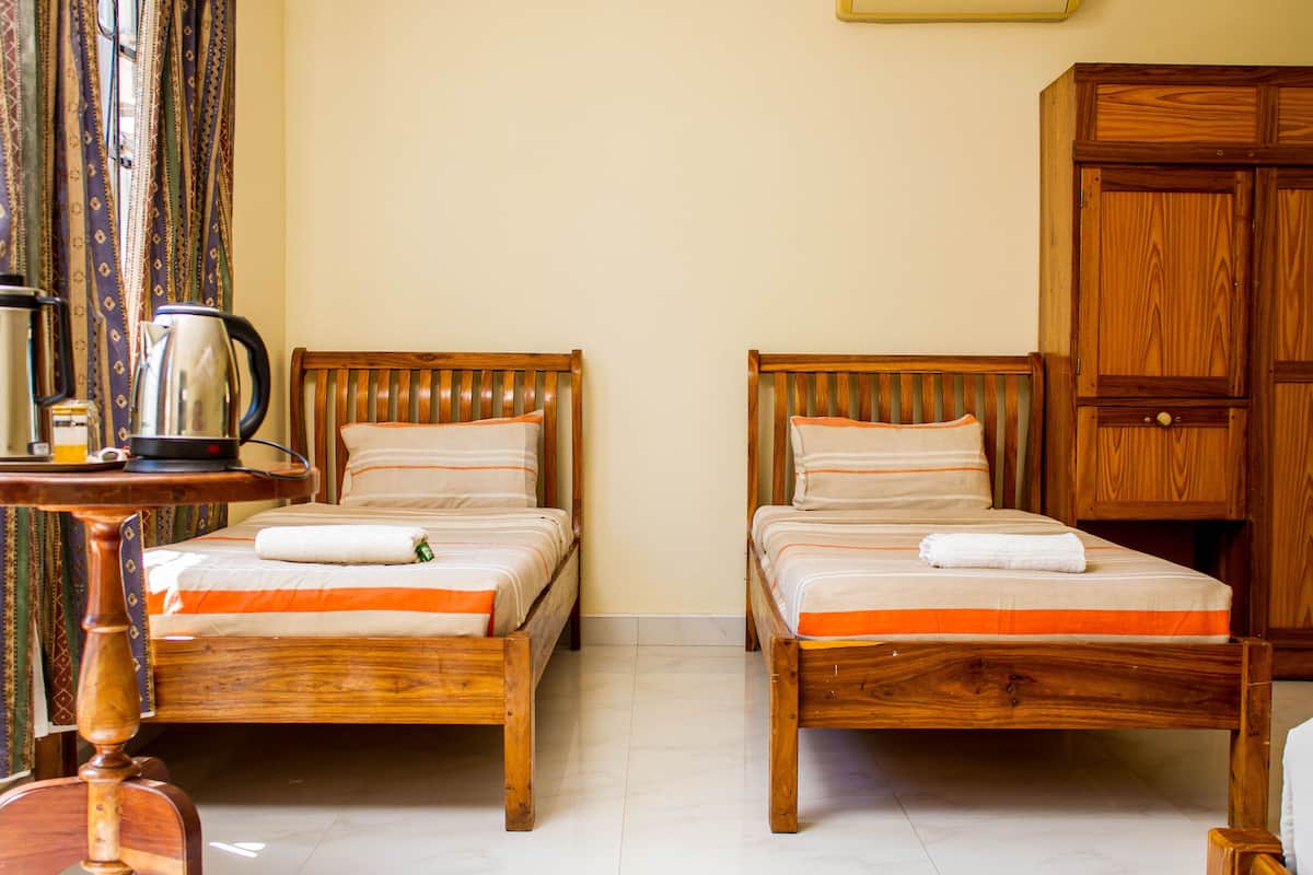 Quarto com duas camas de madeira, um guarda-roupa de madeira e uma mesa com chaleira.