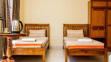 A room with two wooden beds, a wooden wardrobe, and a table with a kettle.
