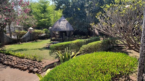 Un jardín con una estructura de techo de paja, setos bien cuidados y una variedad de plantas.