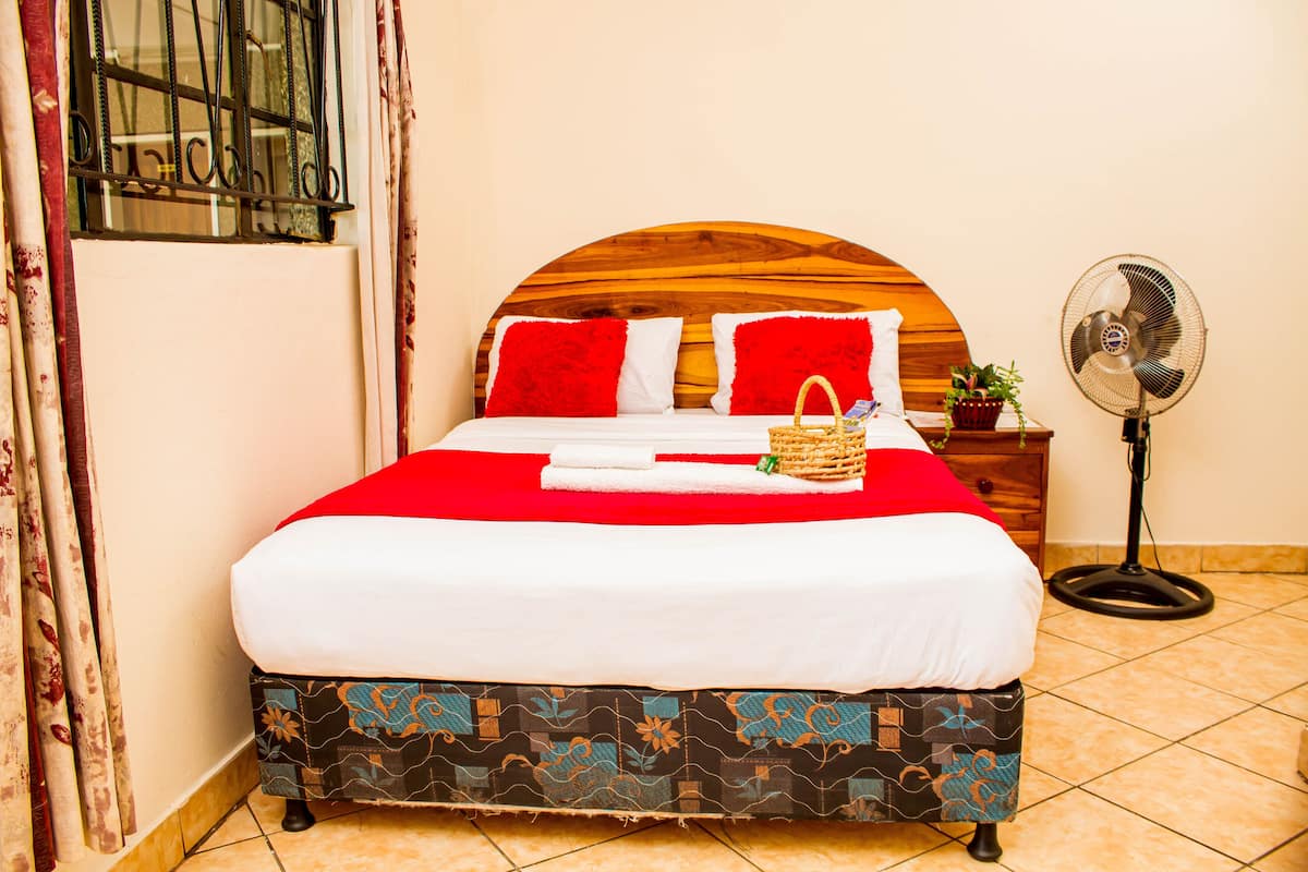 Uma cama bem arrumada com colcha vermelha e branca, uma cabeceira de madeira e uma mesa de cabeceira com uma planta.