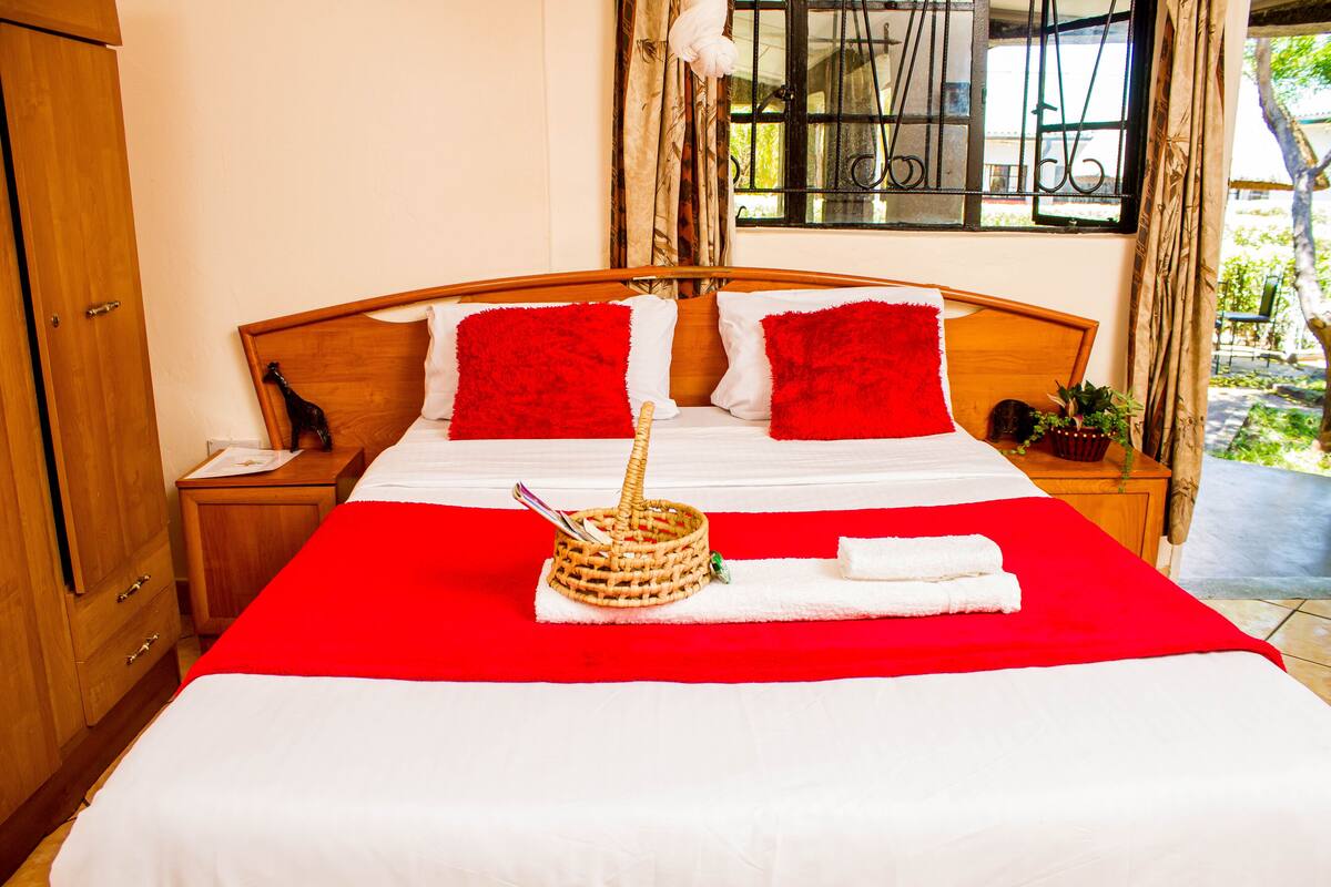 Cama bem arrumada com roupa de cama vermelha e branca, um cesto com uma colher e uma toalha sobre a cama.