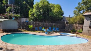 Una piscina con baldosas de piedra, rodeada por una valla de madera y árboles.