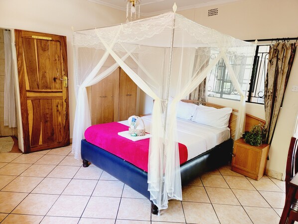 A bedroom with a bed under a canopy, a wooden wardrobe, and a window with curtains. - The Stone Guest House (Livingstone)
