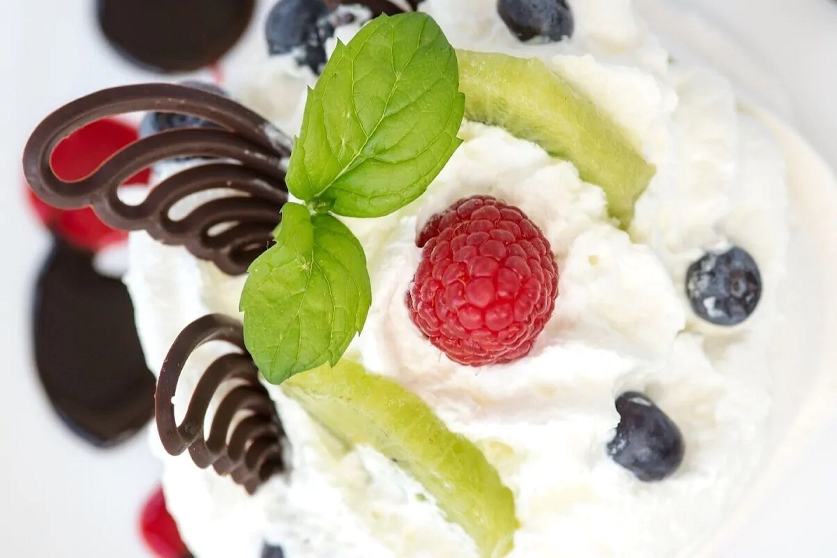 A dessert with whipped cream, raspberries, blueberries, and chocolate curls.