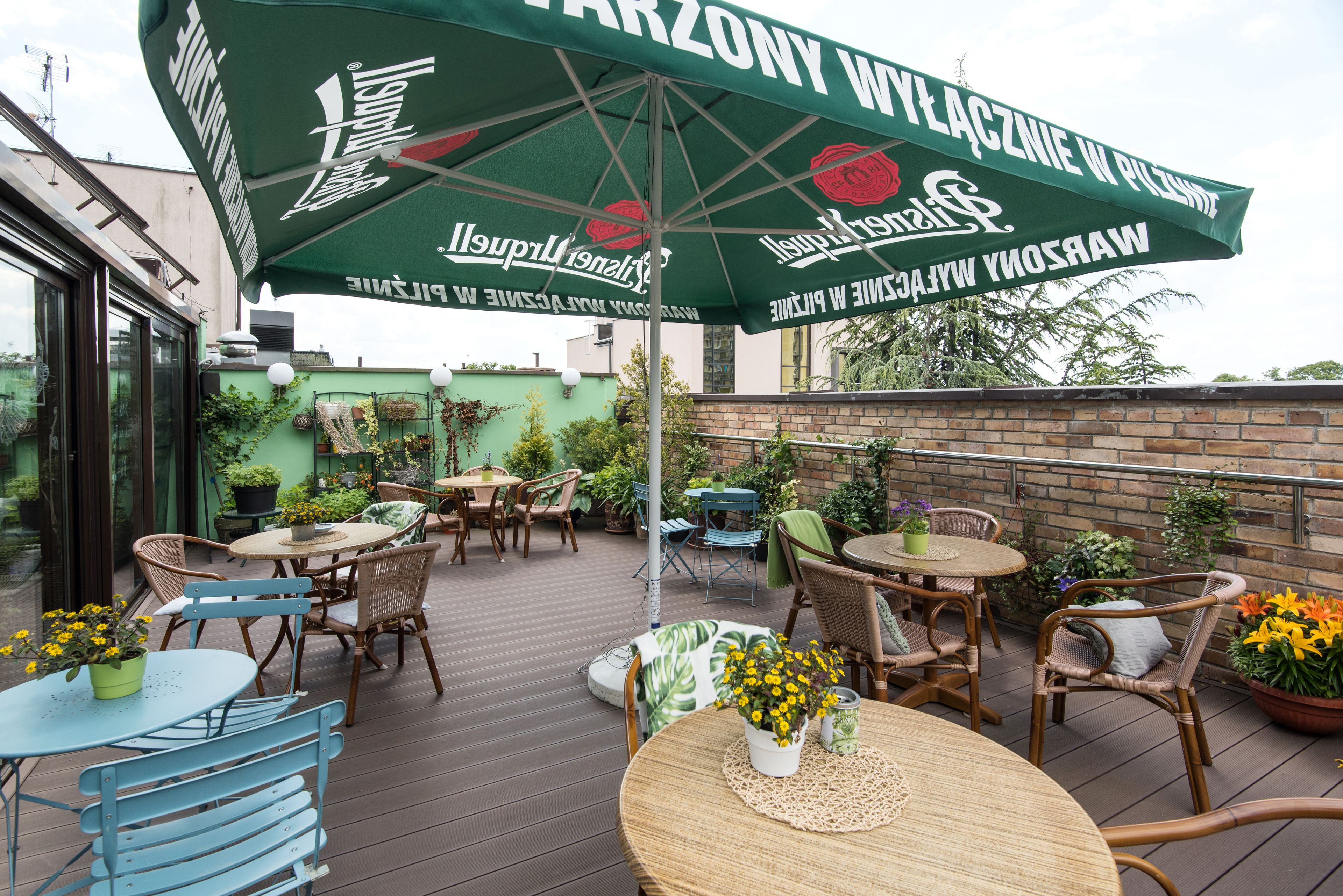 An outdoor patio area with multiple tables and chairs, a large umbrella, and potted plants.