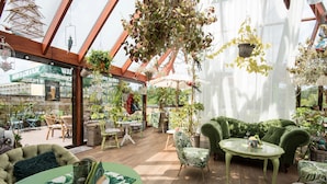 Ein Wintergarten mit Holzdielenboden, grünen Polstermöbeln und hängenden Pflanzen.