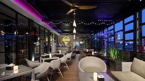 An outdoor seating area with wicker furniture, a bar, and large windows overlooking the city. - Sawana Suites (Jakarta)