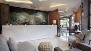 A modern hotel lobby with a marble reception desk, comfortable seating, and a decorative wall with wavy lines. - Sawana Suites (Jakarta)
