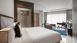 A modern hotel room with a large bed, a desk, a chair, and a bathroom visible through an open door. - Sawana Suites (Jakarta)