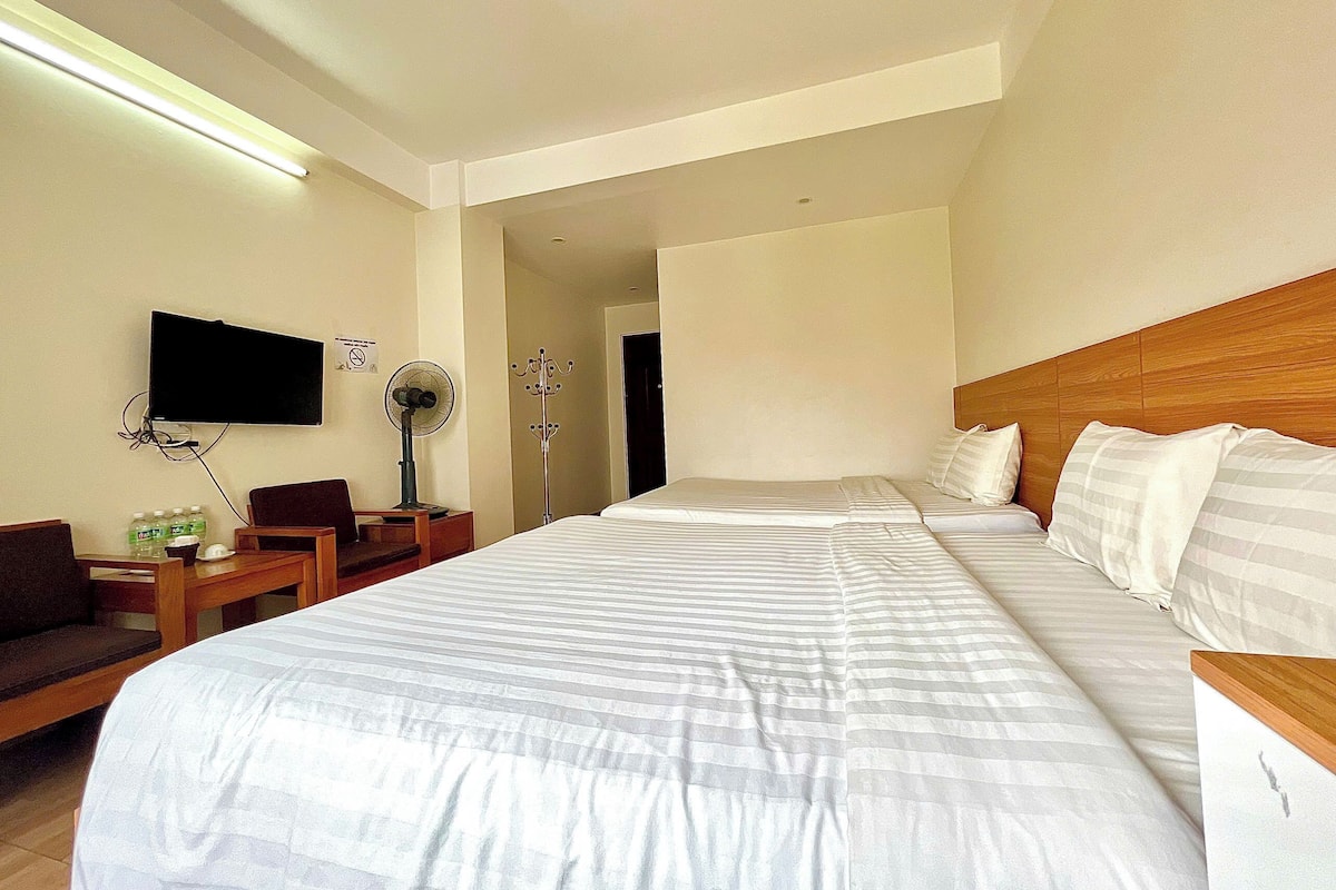 A hotel room with a large bed, a TV mounted on the wall, a desk with a chair, and a coat rack.