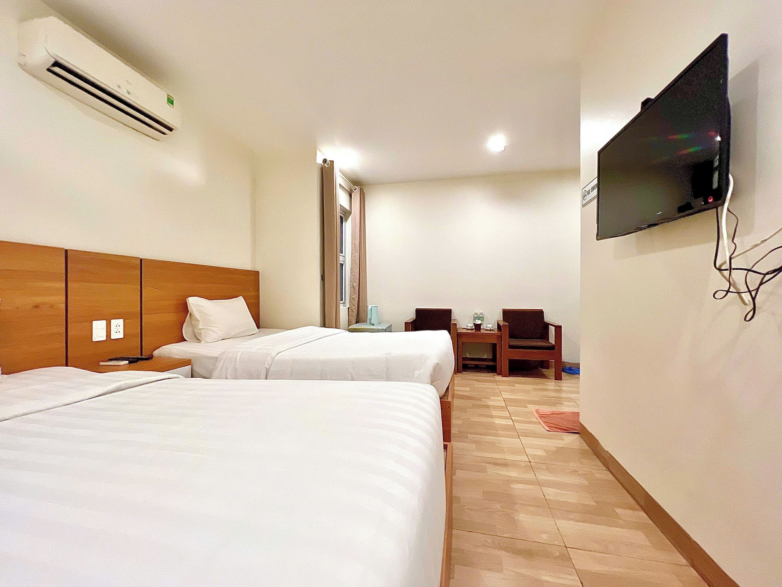 Una habitación de hotel con dos camas, un televisor montado en la pared y una pequeña mesa con sillas.