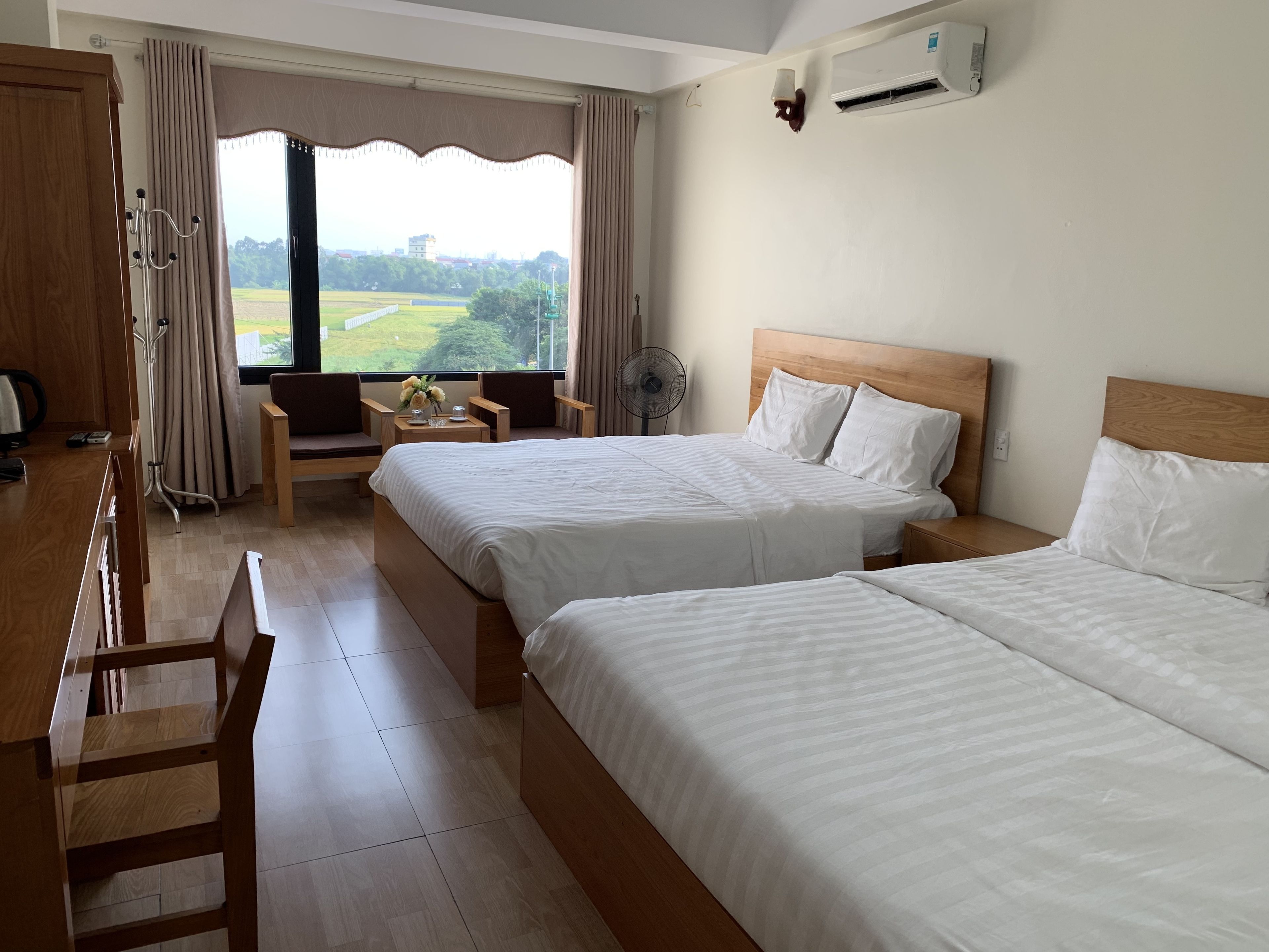 Habitación de hotel con dos camas, un escritorio, una silla, un ventilador y vistas a un paisaje verde.