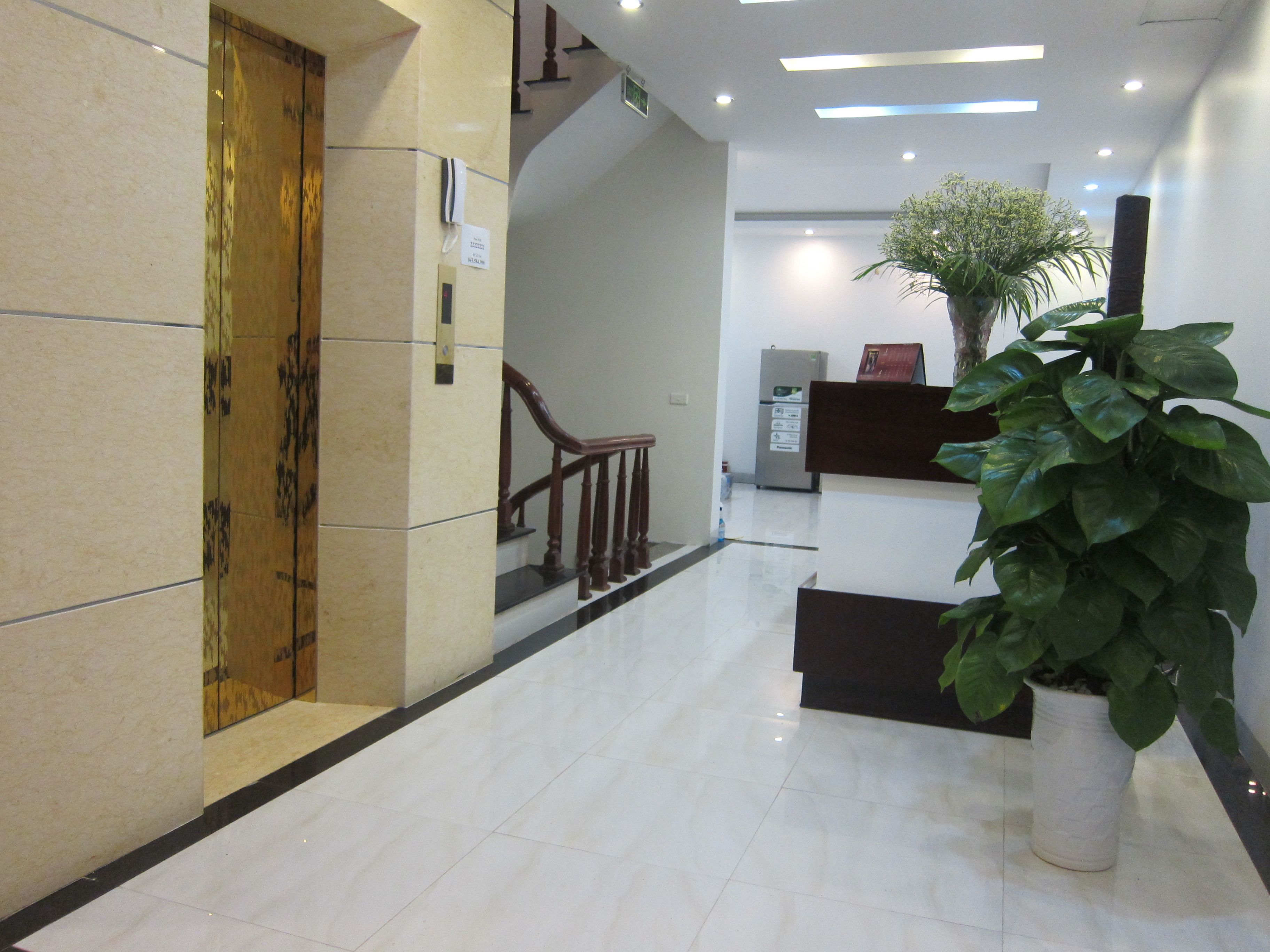 A clean, modern lobby with a reception desk, a staircase, and a potted plant.