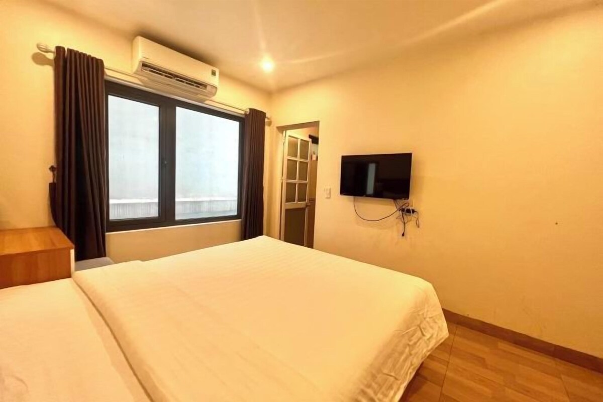 Habitación de hotel con una cama, un equipo de aire acondicionado, un televisor montado en la pared y una ventana con cortinas.