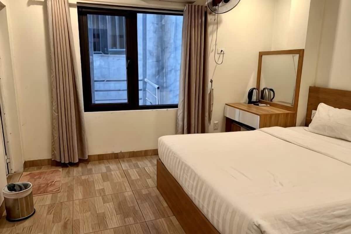 A hotel room with a bed, a bedside table, a mirror, a window with curtains, and a view of the outside.