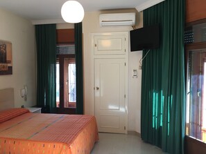Habitación de hotel con una cama, un televisor montado en la pared, una puerta y una ventana con cortinas.