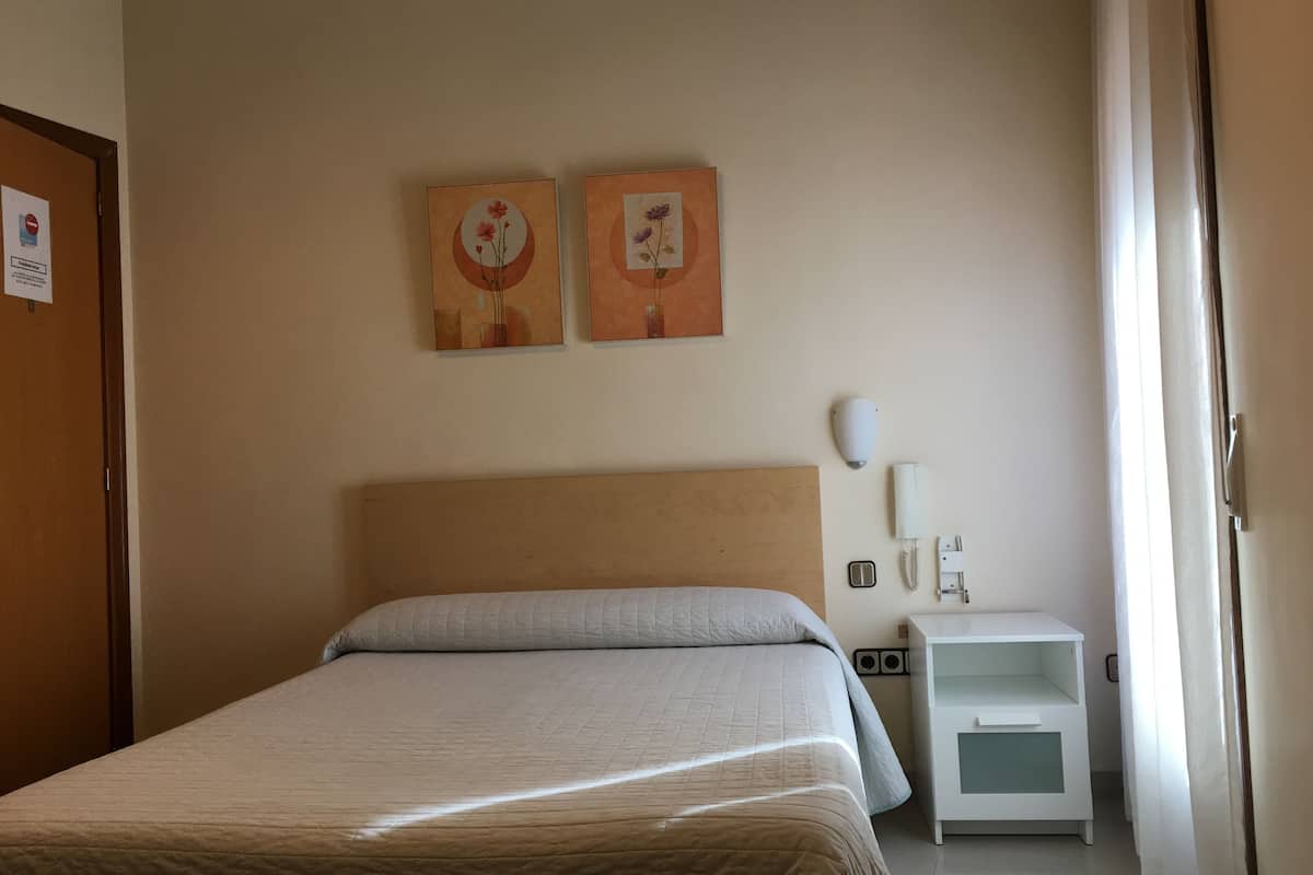 A hotel room with a bed, a nightstand, a phone, and two wall-mounted paintings.