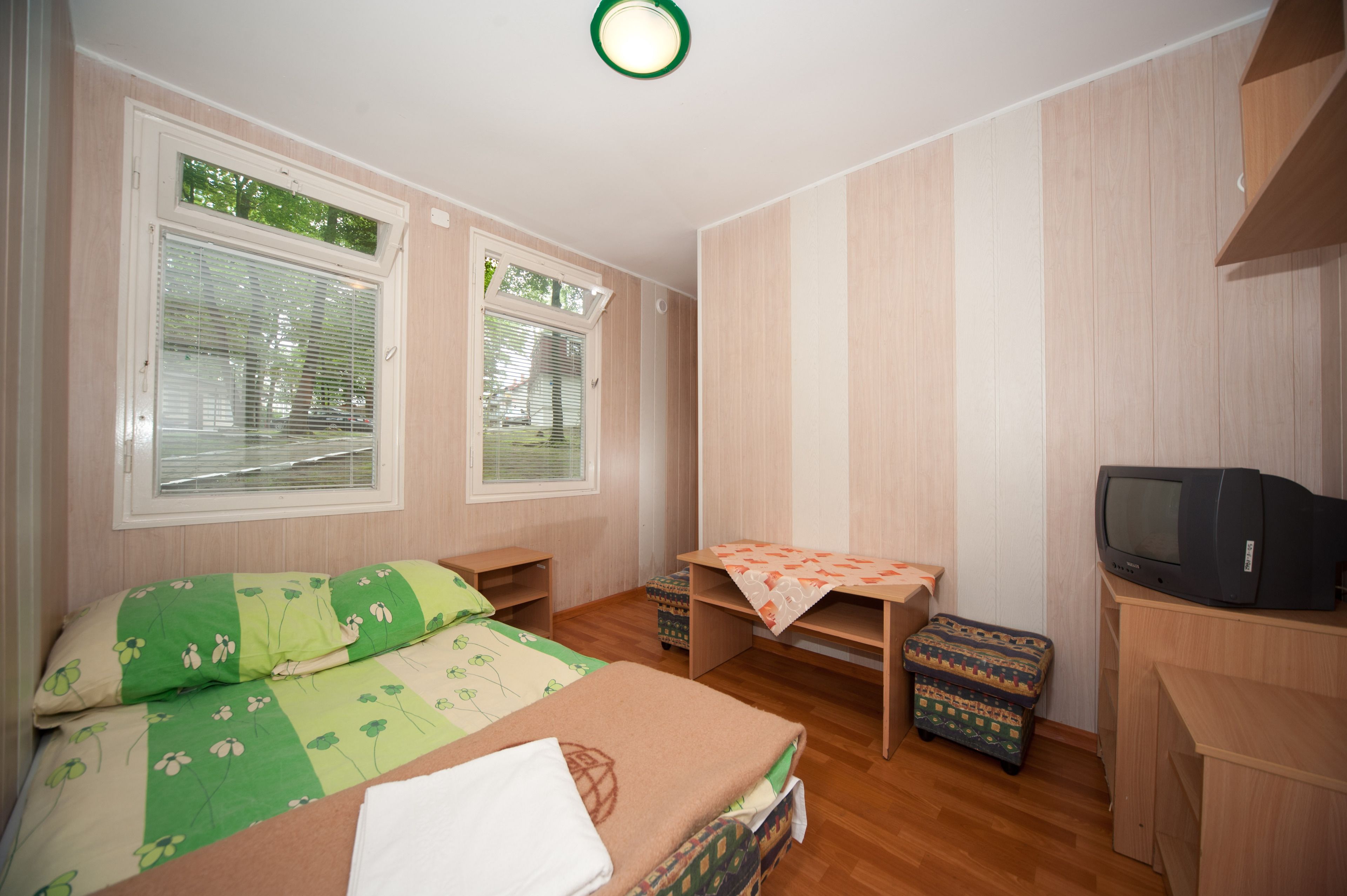 Un dormitorio con cama, televisor, escritorio y ventana.