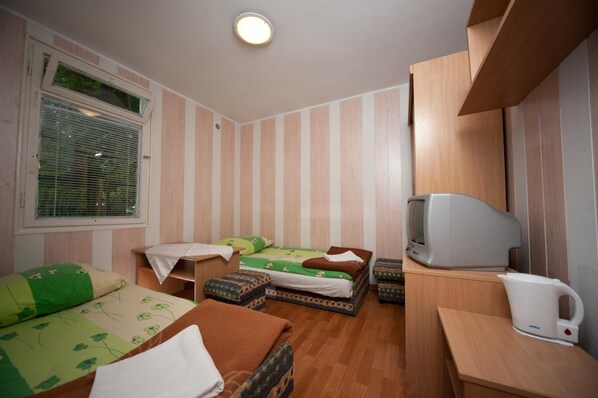 Une chambre d’hôtel compacte avec deux lits simples, une petite télévision, une bouilloire et une fenêtre équipée de stores.