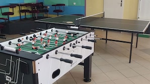 Une pièce avec une table de baby-foot, une table de ping-pong et une porte au fond.
