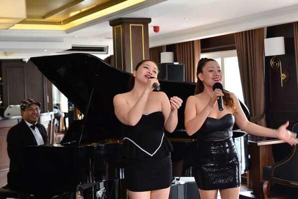 Two women performing on stage with a grand piano in a hotel lobby. - Paradise Elegance Cruise (Tuan Chau)