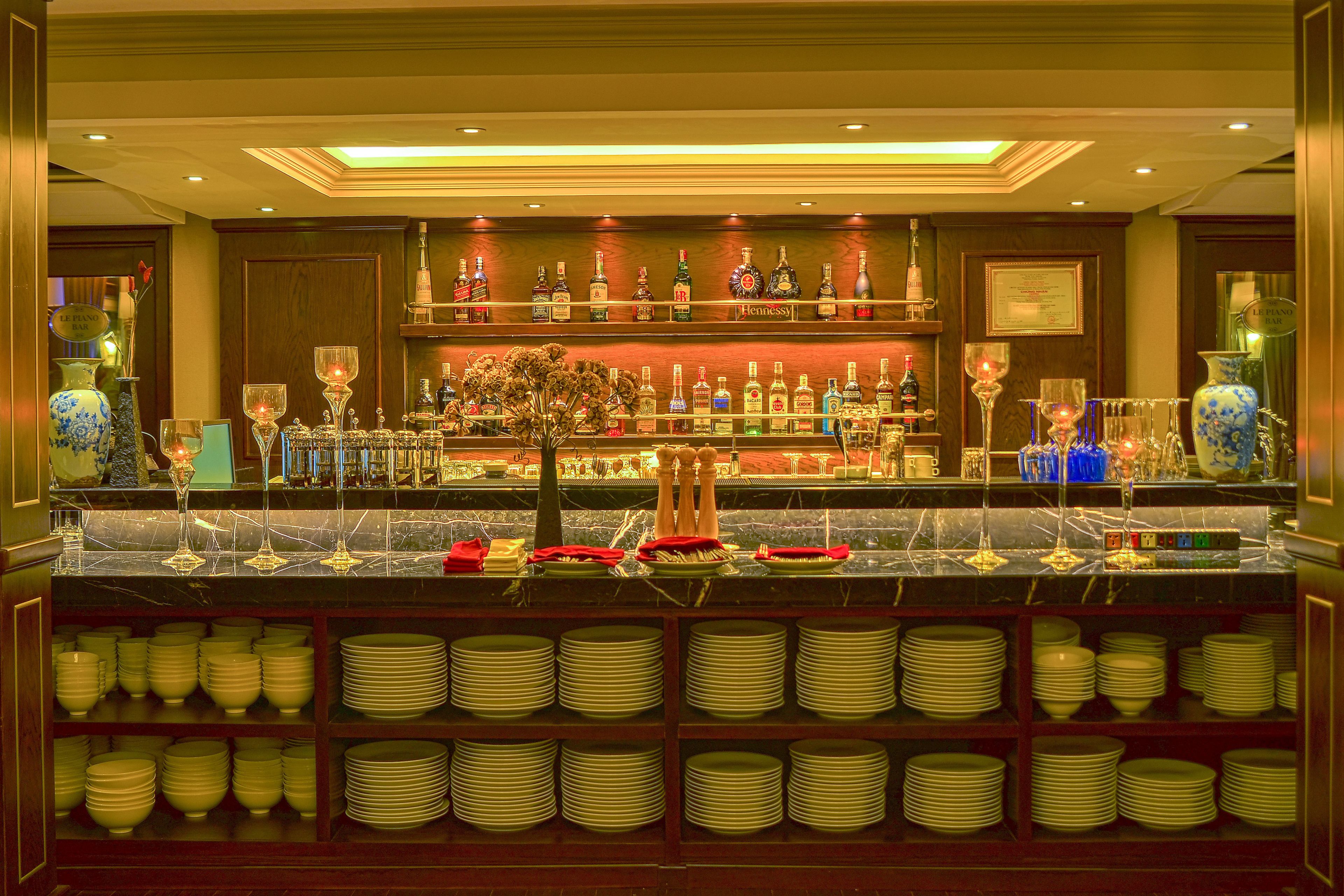 A bar area with shelves of liquor bottles, a marble countertop, and stacks of plates.