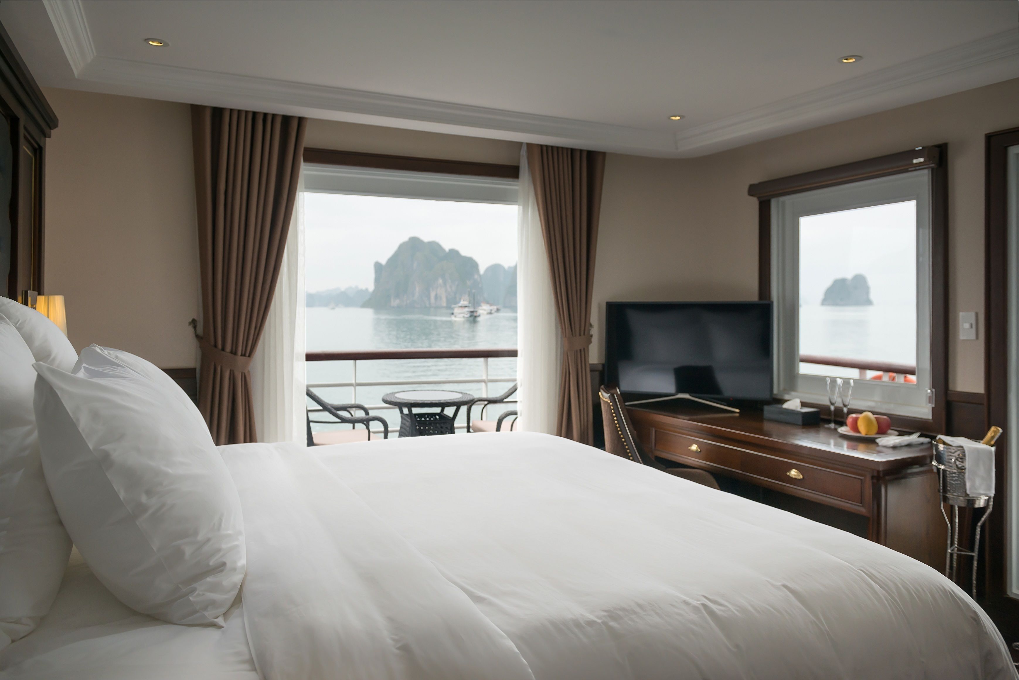 A hotel room with a large bed, a TV, a desk, and a view of the sea.