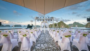 A wedding ceremony setup on a boat deck with white chairs and a floral arch. - Paradise Elegance Cruise (Tuan Chau)