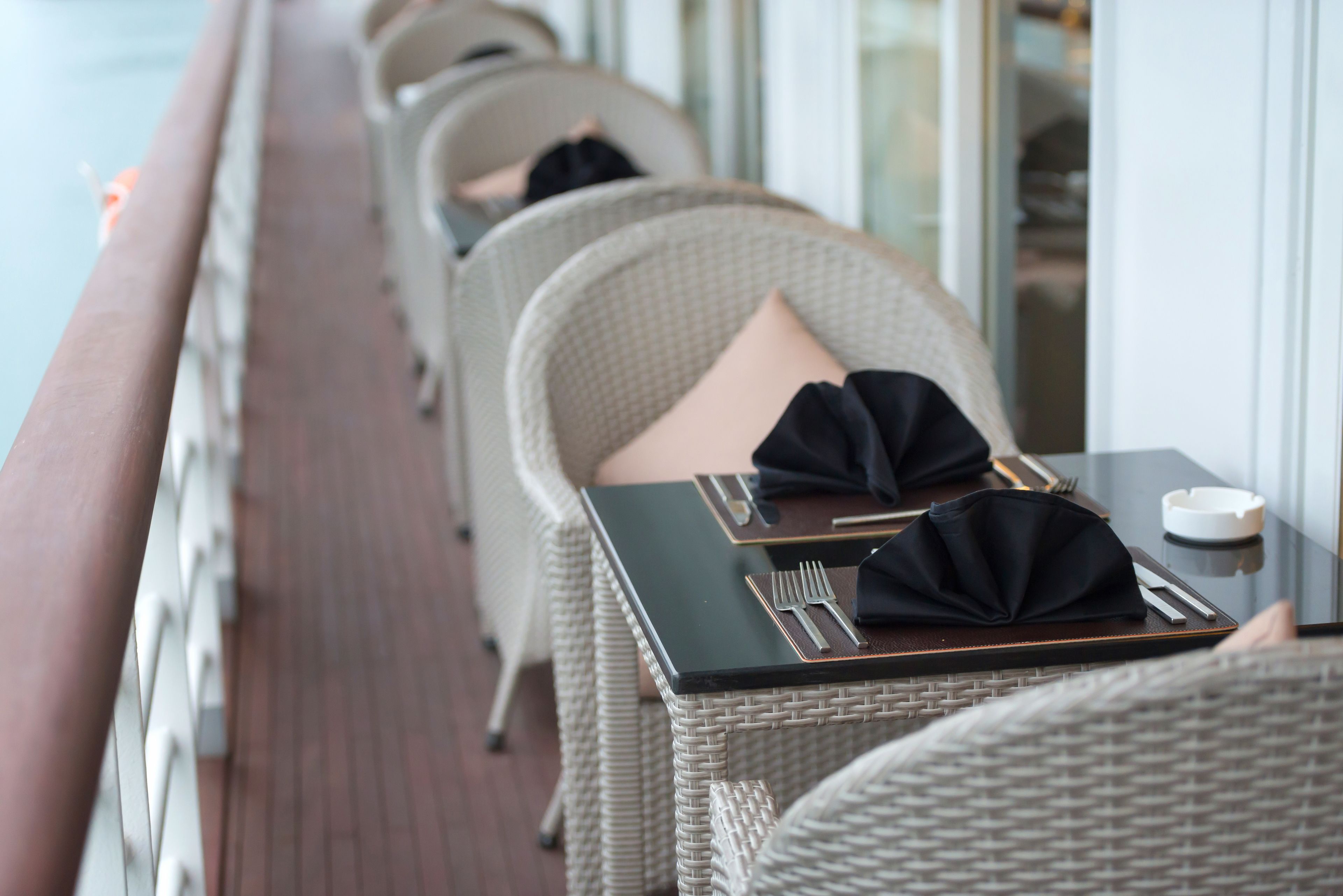 A row of wicker chairs with black napkins and cutlery on a table, suggesting a dining area on a ship.