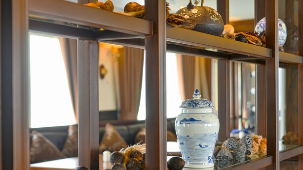 A shelf with decorative items including a white vase with blue patterns, a golden ornament, and various small figurines. - Paradise Elegance Cruise (Tuan Chau)