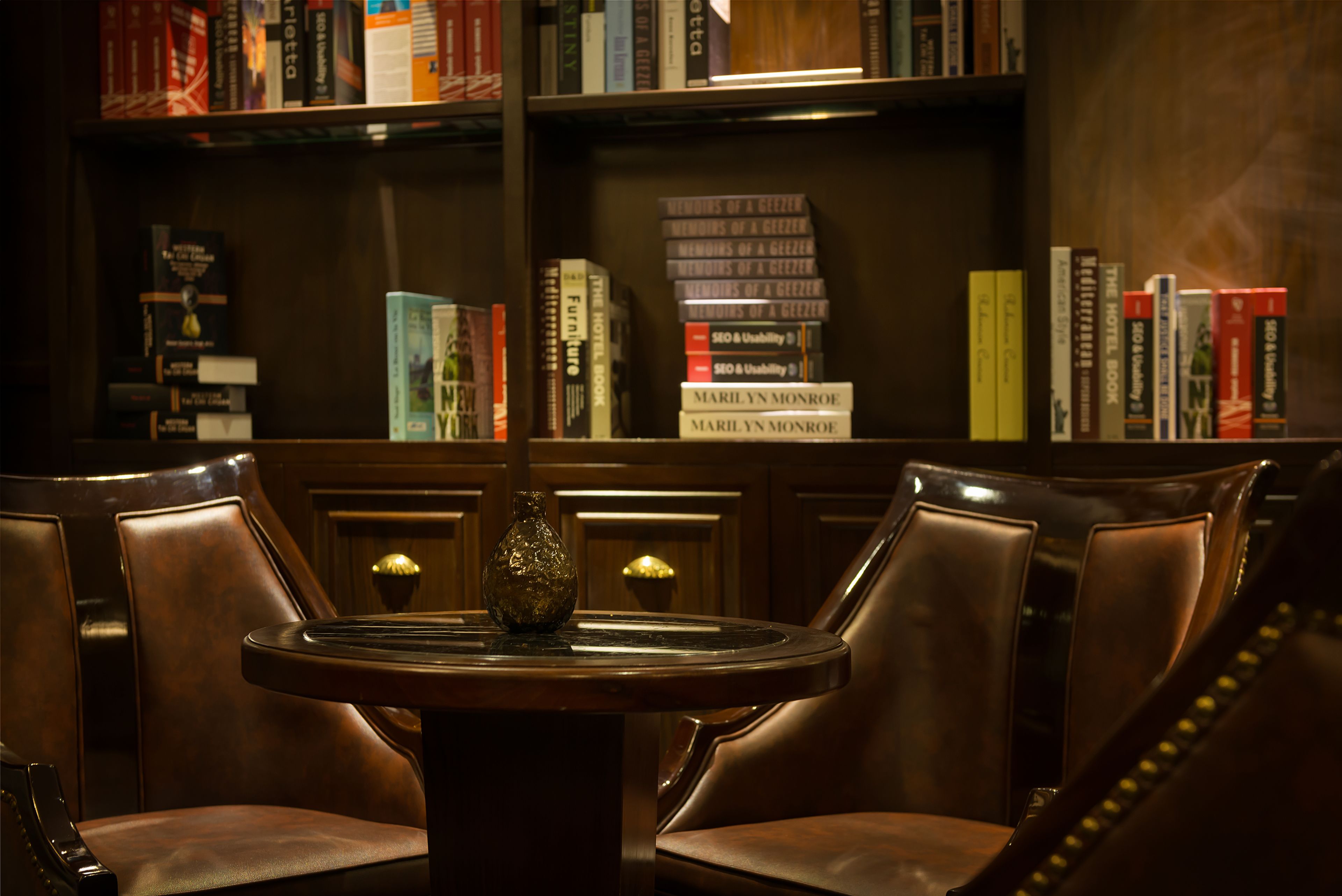 A library with leather chairs and a table, surrounded by bookshelves filled with books.