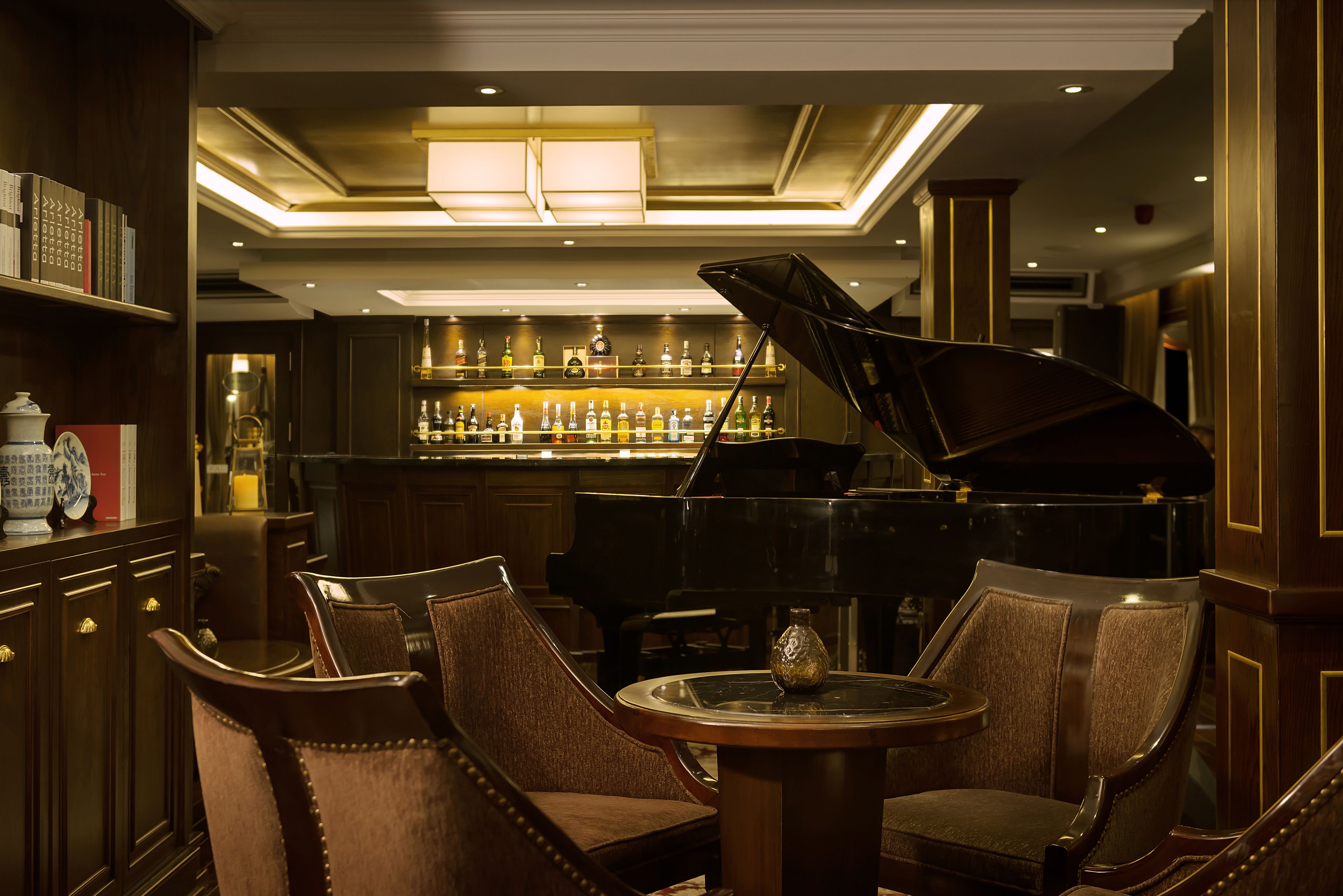 A bar area with a grand piano, bar stools, and a round table with a vase.