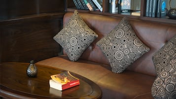 A leather sofa with patterned cushions, a small table with a book and a vase, and a bookshelf in the background.