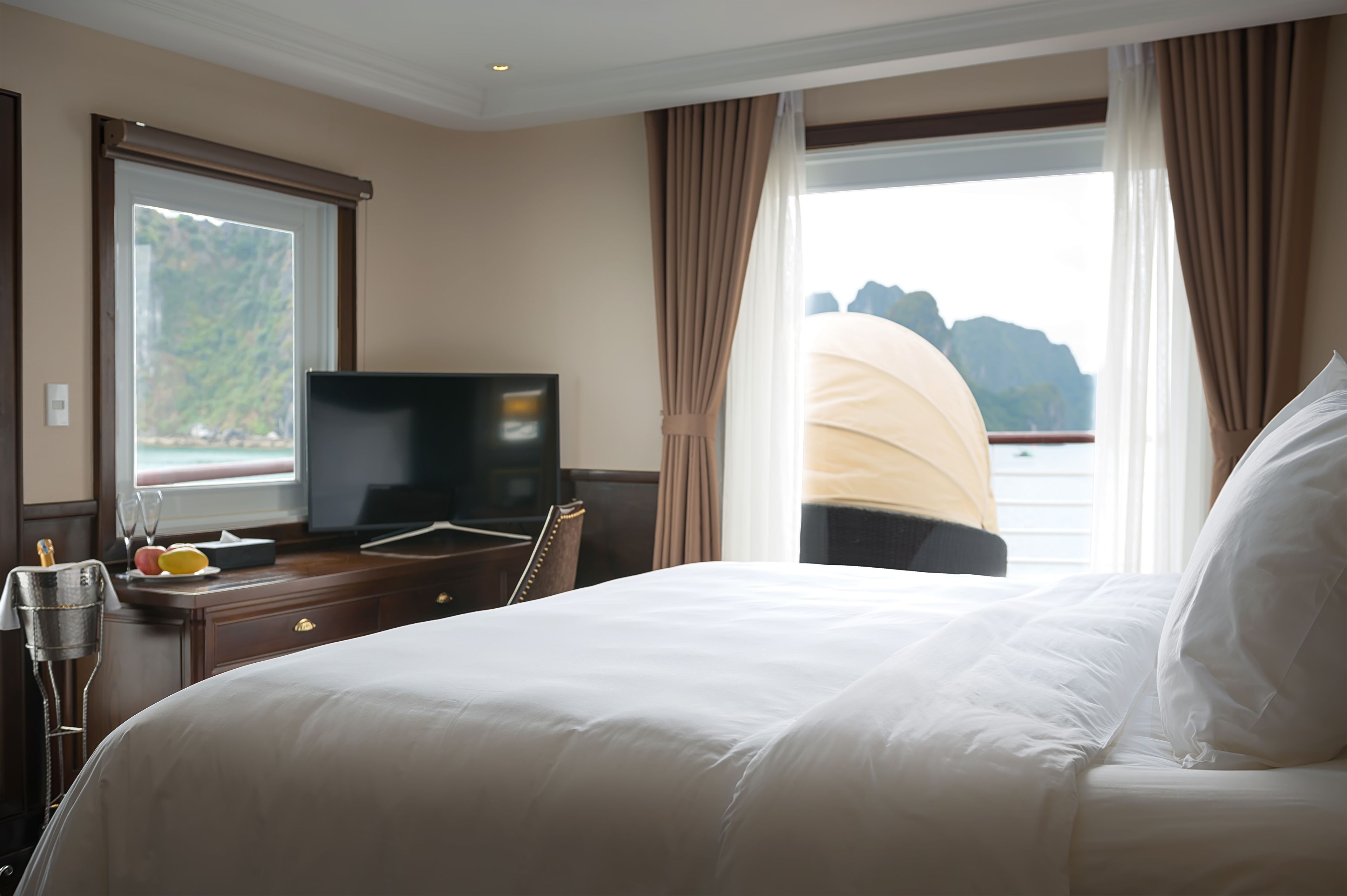 A hotel room with a bed, a desk with a television, and a view of the sea.
