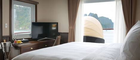 A hotel room with a bed, a desk with a television, and a view of the sea.