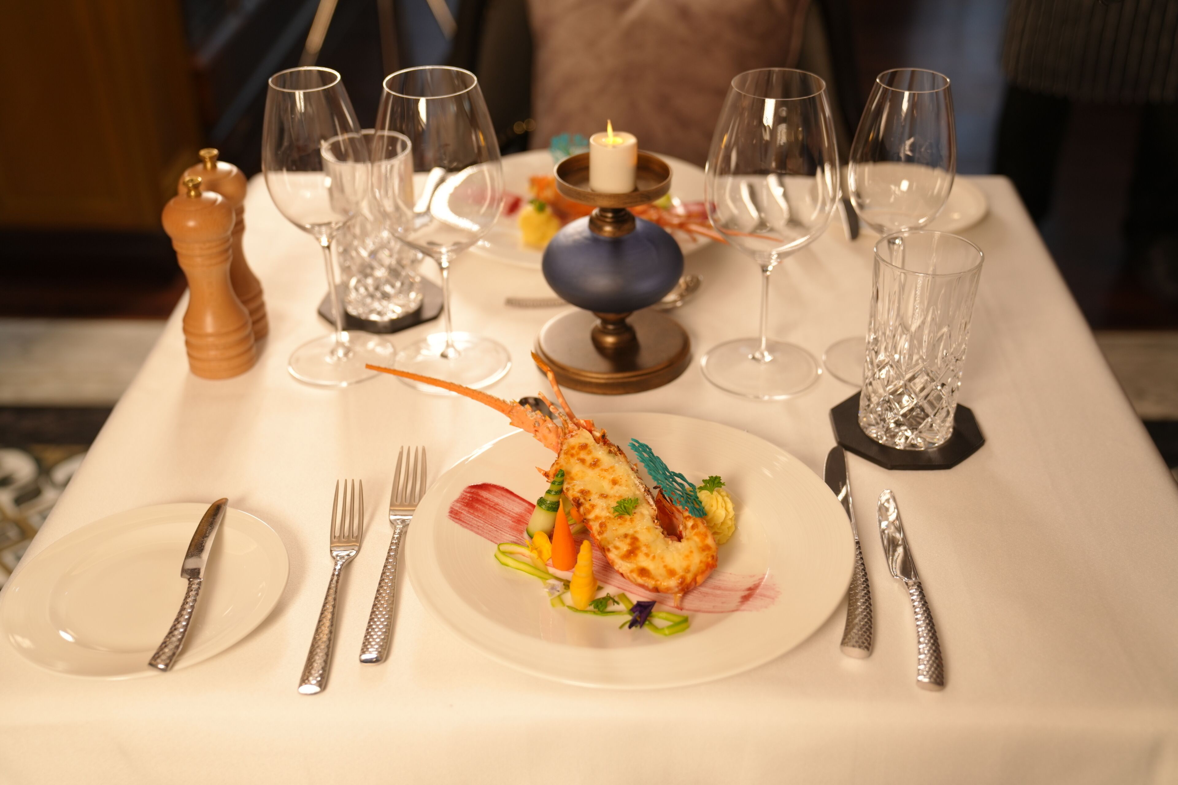 Una mesa de comedor servida con un plato de langosta, copas de vino y cubiertos.