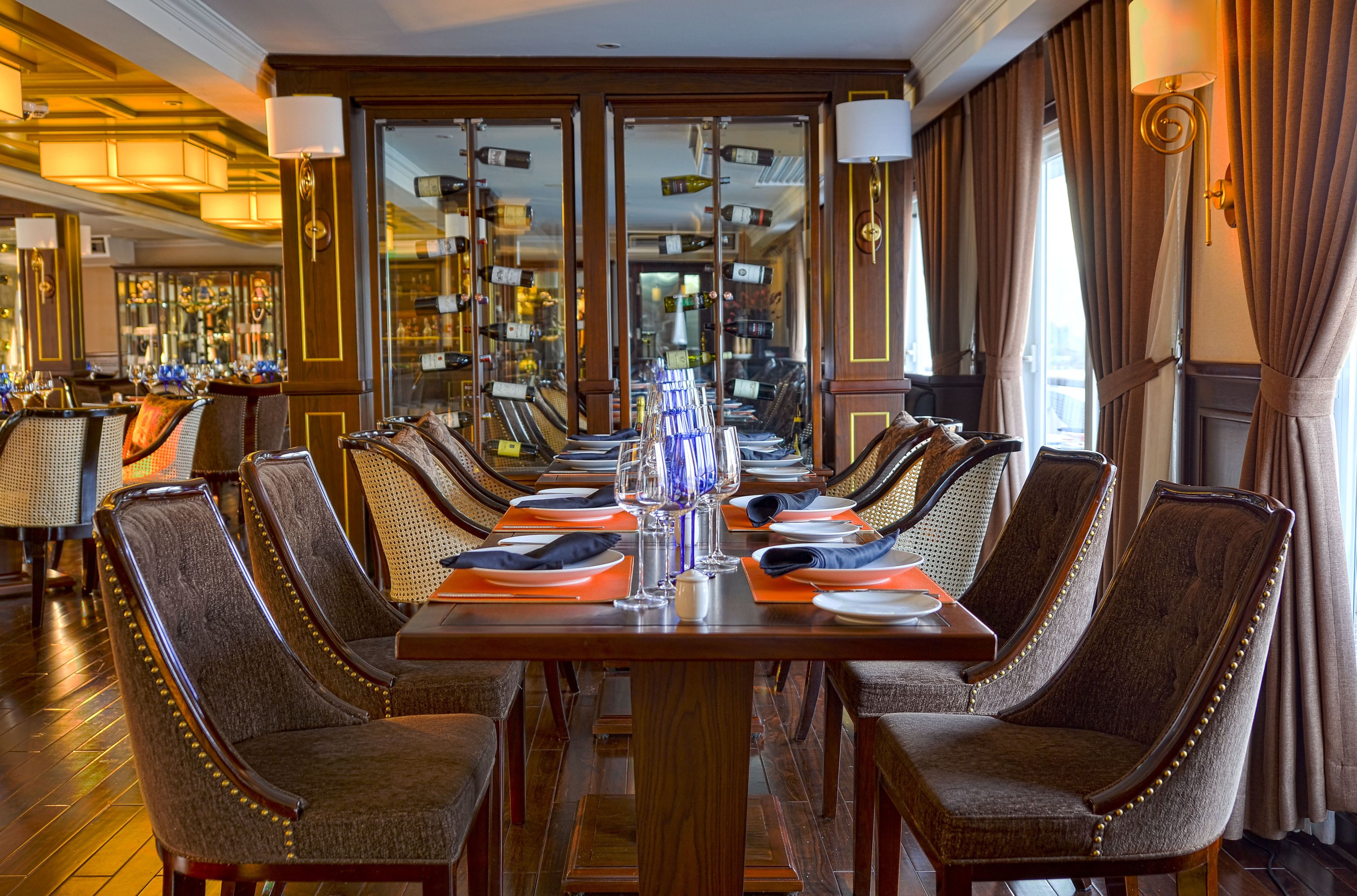 A formal dining room with a long table set for a meal, surrounded by upholstered chairs with gold detailing.