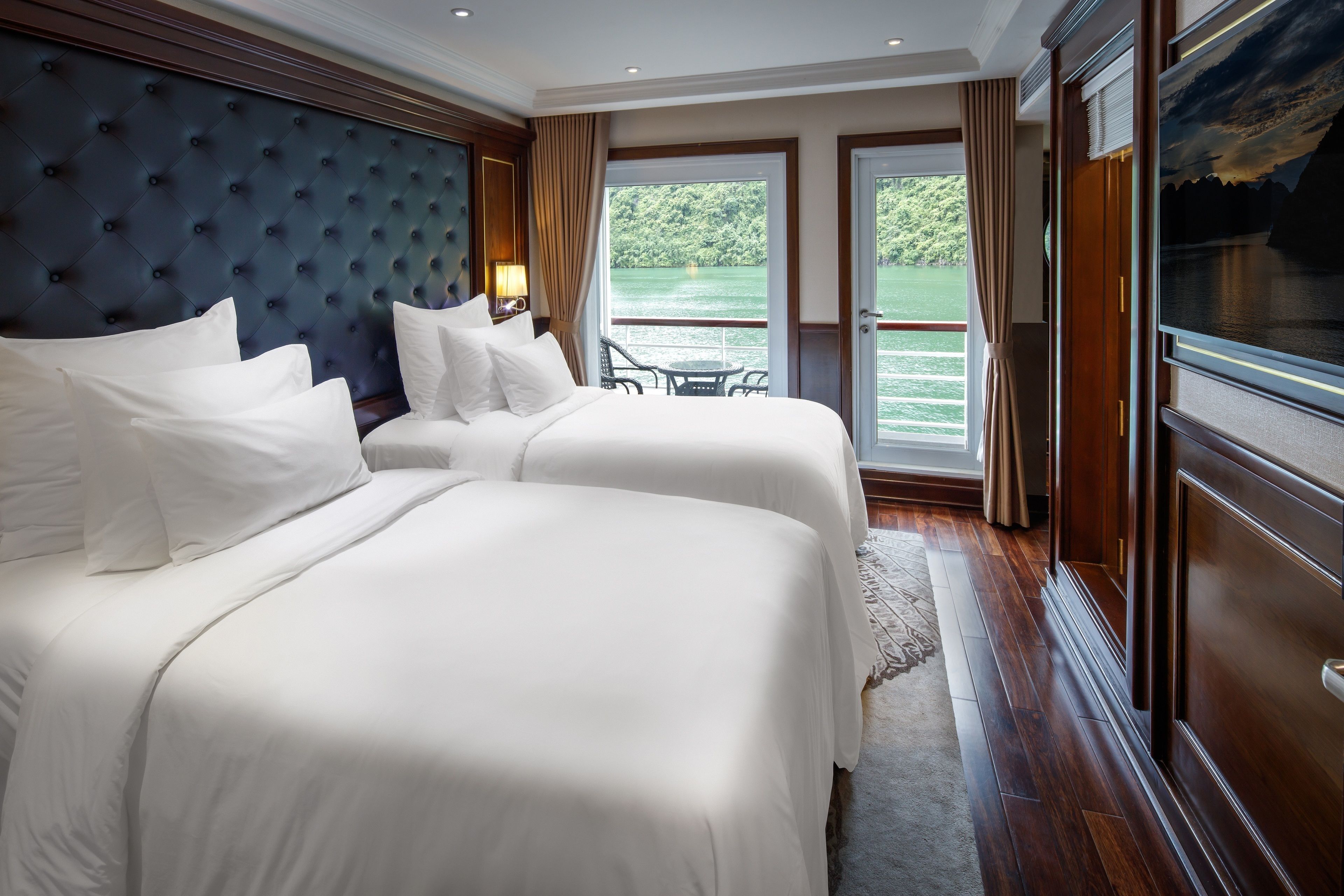 A hotel room with two beds, a large window with a view of a lake, and a balcony with a chair.