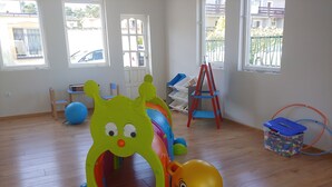 A room with a play area including a slide, a ball pit, and a toy with a slide. There are windows, a chair, and a ladder.
