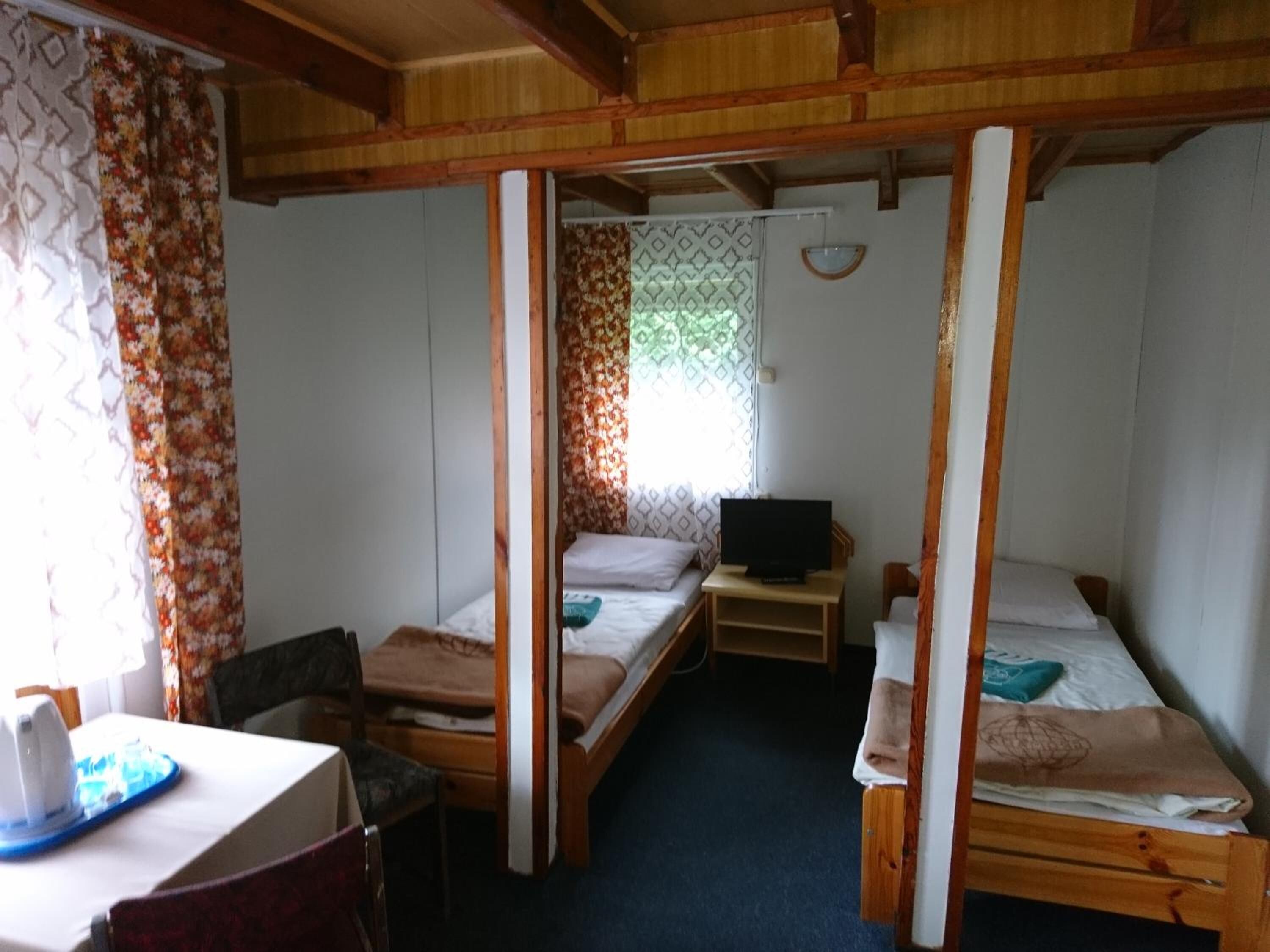 Une petite chambre confortable avec deux lits simples, un bureau en bois, une chaise et un téléviseur.