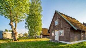 A wooden building with a sloped roof, surrounded by grass and trees.