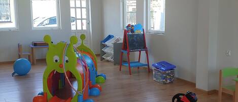A spacious room with wooden flooring, large windows, and a play area with colorful toys.