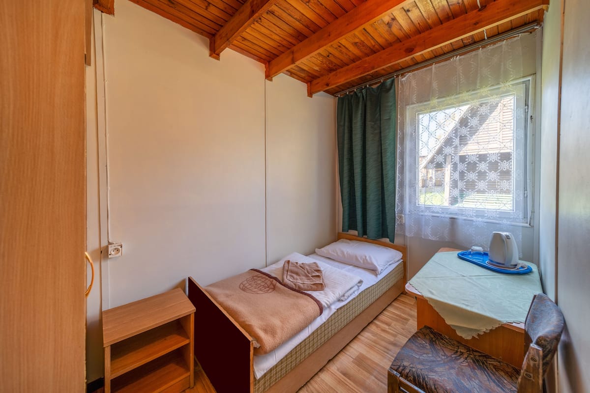 A small, cozy room with a single bed, a wooden desk with a chair, and a window with curtains.