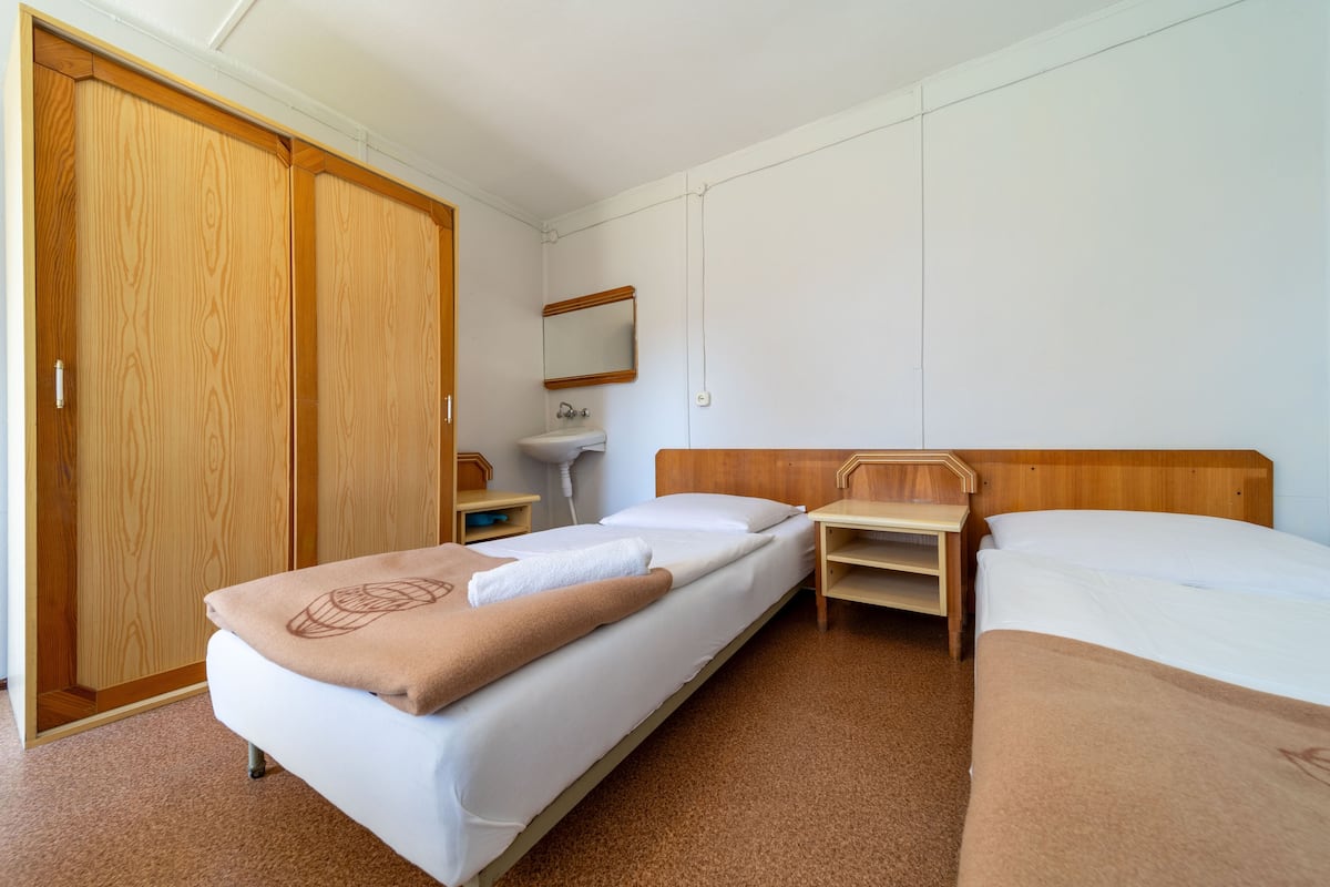 A hotel room with two beds, a wooden wardrobe, a bedside table, a mirror, and a bathroom with a sink.