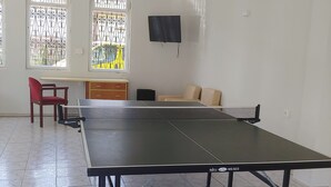 A room with a ping pong table, a TV mounted on the wall, and a window with decorative iron bars.